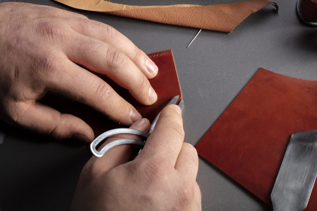 The process of making leather goods. The hands of the master work with a leather product.